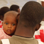Foto: Ein haitianisches Baby schaut über die Schulder eines Rotkreuzhelfers.