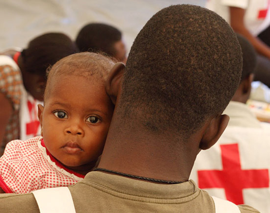 Foto: Ein haitianisches Baby schaut über die Schulder eines  Rotkreuzhelfers.