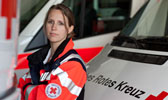 Foto: Eine Rettungssanitäterin steht zwischen Einsatzwägen. Dieses Foto ist gleichzeitig ein Link und führt Sie zu der Unterseite: First Responder.